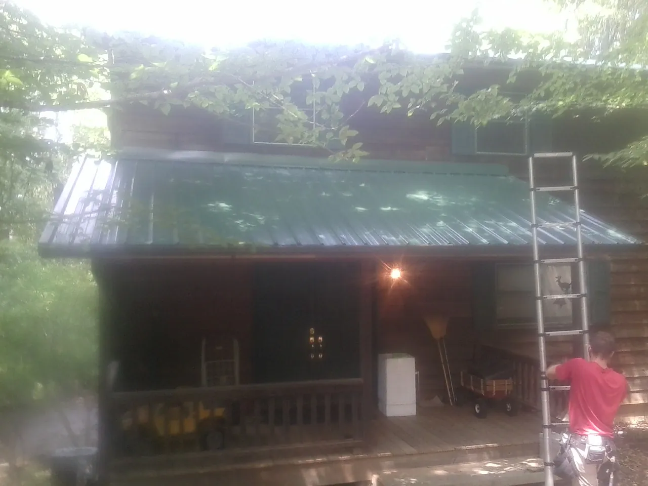 Worker on a ladder at the green porch roof of a wooded cabin in Brandon