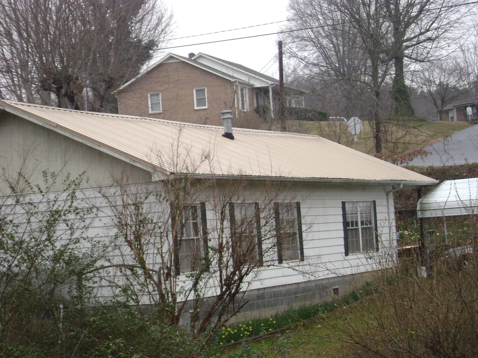 Tan metal roof on a white sided house set into a hillside — Commercial Roofing by Roofing Brothers in Brandon